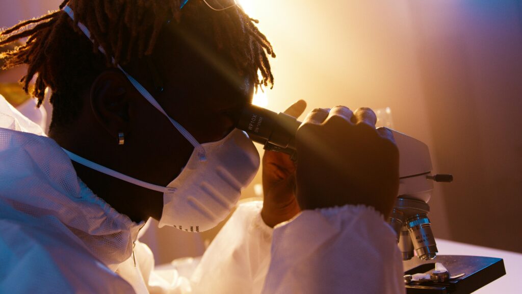 Scientist wearing protective gear examining samples under a microscope in a laboratory.